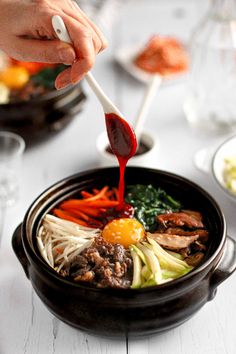 a person is dipping sauce on some food in a bowl with vegetables and meats