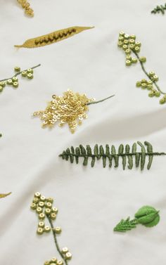 some gold and green flowers on a white cloth with leaves, beads and other things