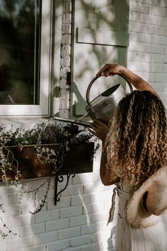 a woman with curly hair pouring water from a watering can into a window sill