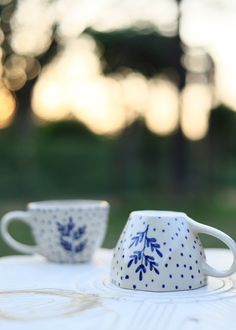 two blue and white cups sitting on top of a table with trees in the background