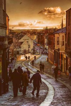 people are walking down the street in an old town at sunset or sunrise, with buildings and shops on either side