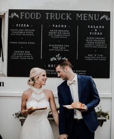 a man and woman standing next to each other in front of a food truck menu