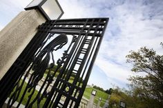 an iron gate with a clock on it in front of a grassy field and blue sky