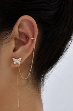 a close up of a person's ear wearing gold chain earrings with butterfly charms