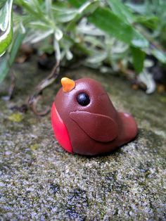 a small toy bird sitting on top of a rock next to some green plant life