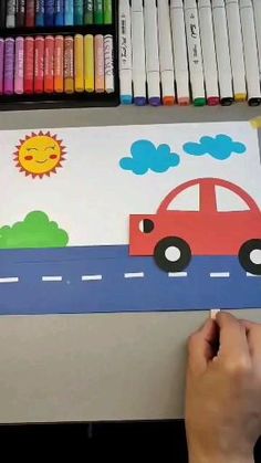 someone is drawing a car on the paper with crayons in front of them