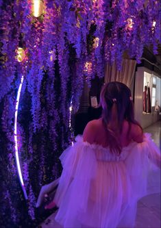 a woman in a white dress is standing under purple wistery trees at night