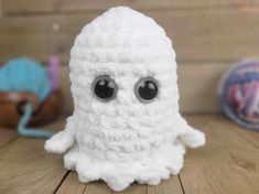 a white stuffed animal sitting on top of a wooden table next to balls of yarn