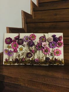 an art piece with flowers painted on it sitting on top of a wooden table next to some stairs