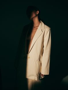 a man standing in the dark with his shirt open and no shirt on, wearing a white blazer