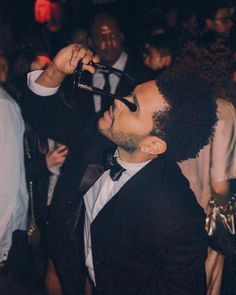 a man in a tuxedo is drinking from a wine glass at a party