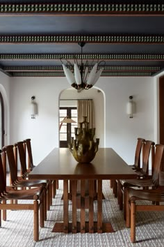 a dining room table with chairs and a vase on the centerpiece in front of it