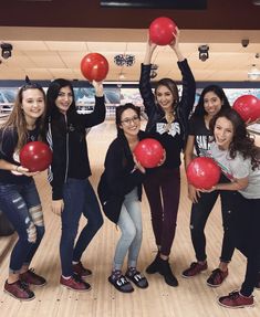 several girls holding up red balls in a bowling alley