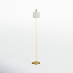 a gold floor lamp with a white shade on the top, and a round base