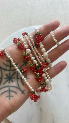 a woman's hand with several bracelets on it, including pearls and red beads