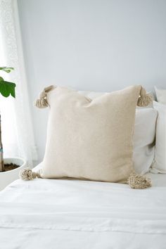 a white bed topped with pillows next to a potted plant