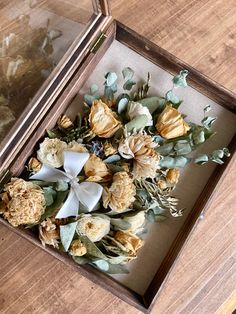 an arrangement of dried flowers in a wooden box on a wood table next to a glass case