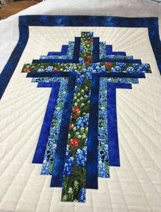 a blue and white quilted cross with flowers on it's sides is laying on a table