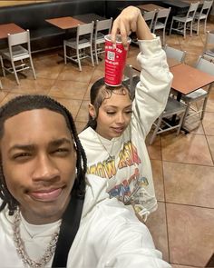 a young man holding up a red cup in front of his head while standing next to a woman