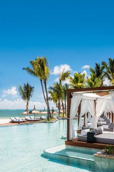 a bed sitting on top of a swimming pool next to palm trees and the ocean