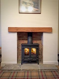 a wood burning stove in a living room with plaid rugs on the floor and a painting above it