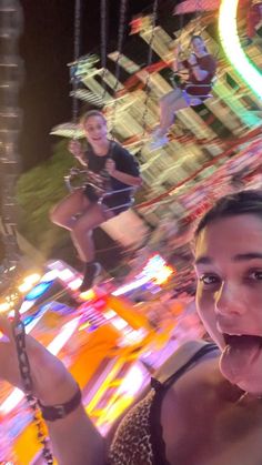 a woman taking a selfie in front of a carnival ride at night with her phone up to her ear