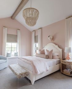 a bedroom decorated in pink and white with a large bed, two chairs, and a chandelier hanging from the ceiling