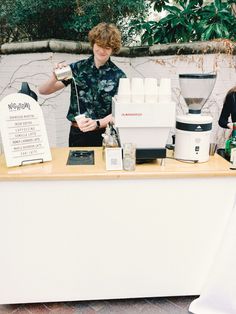 a man standing behind a counter with some bottles on it and a sign in front of him