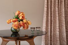 a vase with orange flowers sitting on top of a table next to two wine glasses