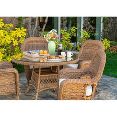 an outdoor dining set with wicker chairs and a glass top table in front of yellow flowers