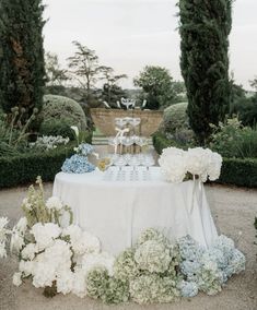 an outdoor table with flowers on it in the middle of some bushes and trees,