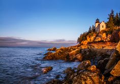 a lighthouse on top of a rocky cliff next to the ocean with trees in the background