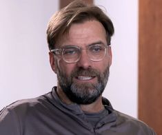 a man with glasses and a beard is looking at the camera while wearing a gray shirt