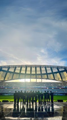 a group of people standing in front of a large stadium with the sun shining down