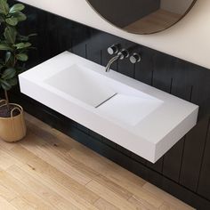 a bathroom sink sitting under a mirror next to a potted plant and wall mounted faucet