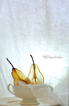 two pears are in a white bowl on a table with the light coming from behind them