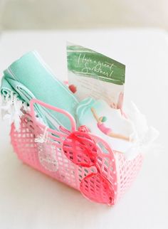 a pink basket filled with lots of items on top of a white table next to a card