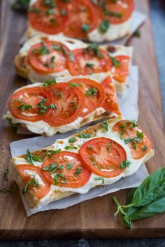 slices of bread topped with tomatoes and cheese on top of a wooden cutting board next to basil leaves