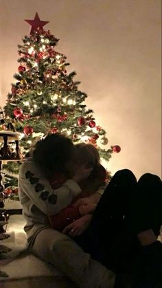 two people sitting in front of a christmas tree