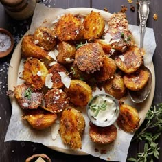 some fried potatoes on a plate with ranch dressing and herbs next to the side dish