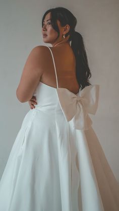 a woman in a white dress with a big bow on her back, looking off to the side