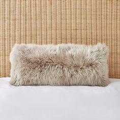 a furry pillow on top of a bed next to a wicker headboard with white sheets