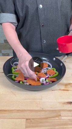 a person cooking food in a frying pan on top of a wooden table next to a red cup