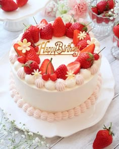 a birthday cake with strawberries and flowers on the top is sitting on a table