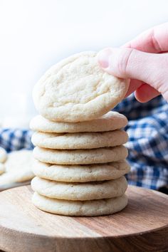 a stack of white cookies sitting on top of a wooden board next to a person