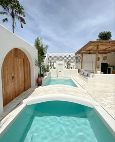 an outdoor swimming pool surrounded by white walls and wooden doors, with blue water in the middle