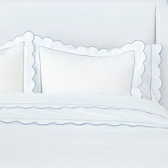 a bed with white sheets and blue scalloped pillows