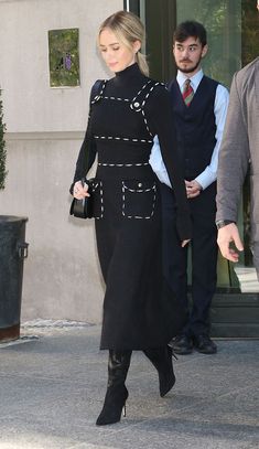 a woman in a black dress is walking down the street with her hand on her hip