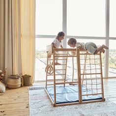 two children are playing on a bed made out of wood and rope, in front of a large window