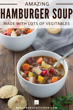 two bowls of hamburger soup on a wooden table with crackers and vegetables in the background